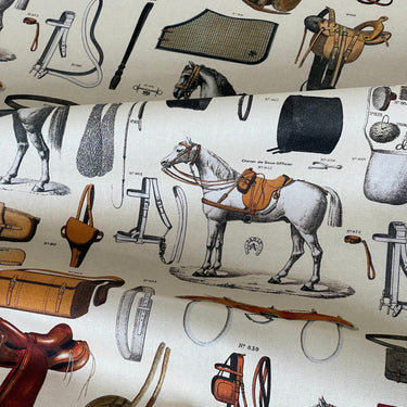 Close-up of vintage equestrian print cotton fabric showing white horses, saddles, bridles, and tack equipment on a cream background – ideal for country upholstery and curtains.